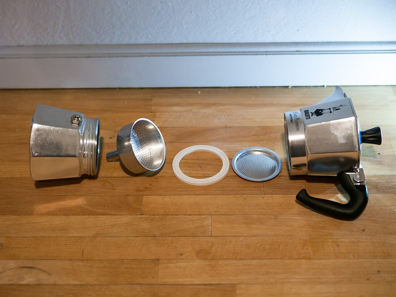 Disassembled Bialetti moka pot with gasket and filter arranged on a wooden surface